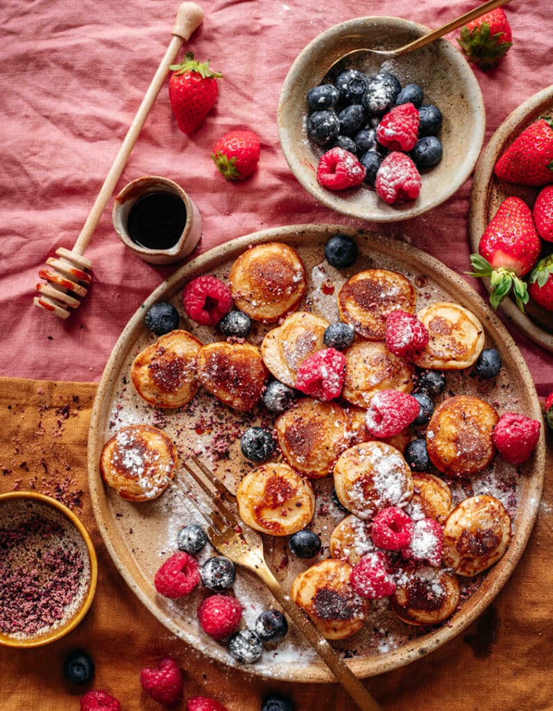 Ein Teller mit frisch gebackenen, Vegane Pancakes verfeinert mit Bio Porridge Food Finisher. Die Pfannkuchen sind locker und fluffig, garniert mit der aromatischen Bio- und veganen Gewürzzubereitung, die aus hochwertigem Hibiskusblüten*, Orangenschalen*, Mangopulver*, getrocknete, gemahlene Datteln*, Tonkabohne* besteht. Ein köstliches Frühstück oder Dessert, das sowohl optisch als auch geschmacklich überzeugt. Das Bild stammt aus einem Rezept von Luis Dias, einem Spitzenkoch.