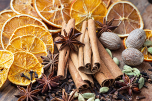 Getrocknete Orangenscheiben, Zimtstangen, Sternanis, Nelken, Muskatnüsse und Kardamomkapseln auf Holz – klassische Weihnachtsgewürze in der Nahaufnahme.
